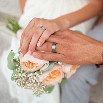 Two hands wearing wedding rings placed on a bouquet of flowers