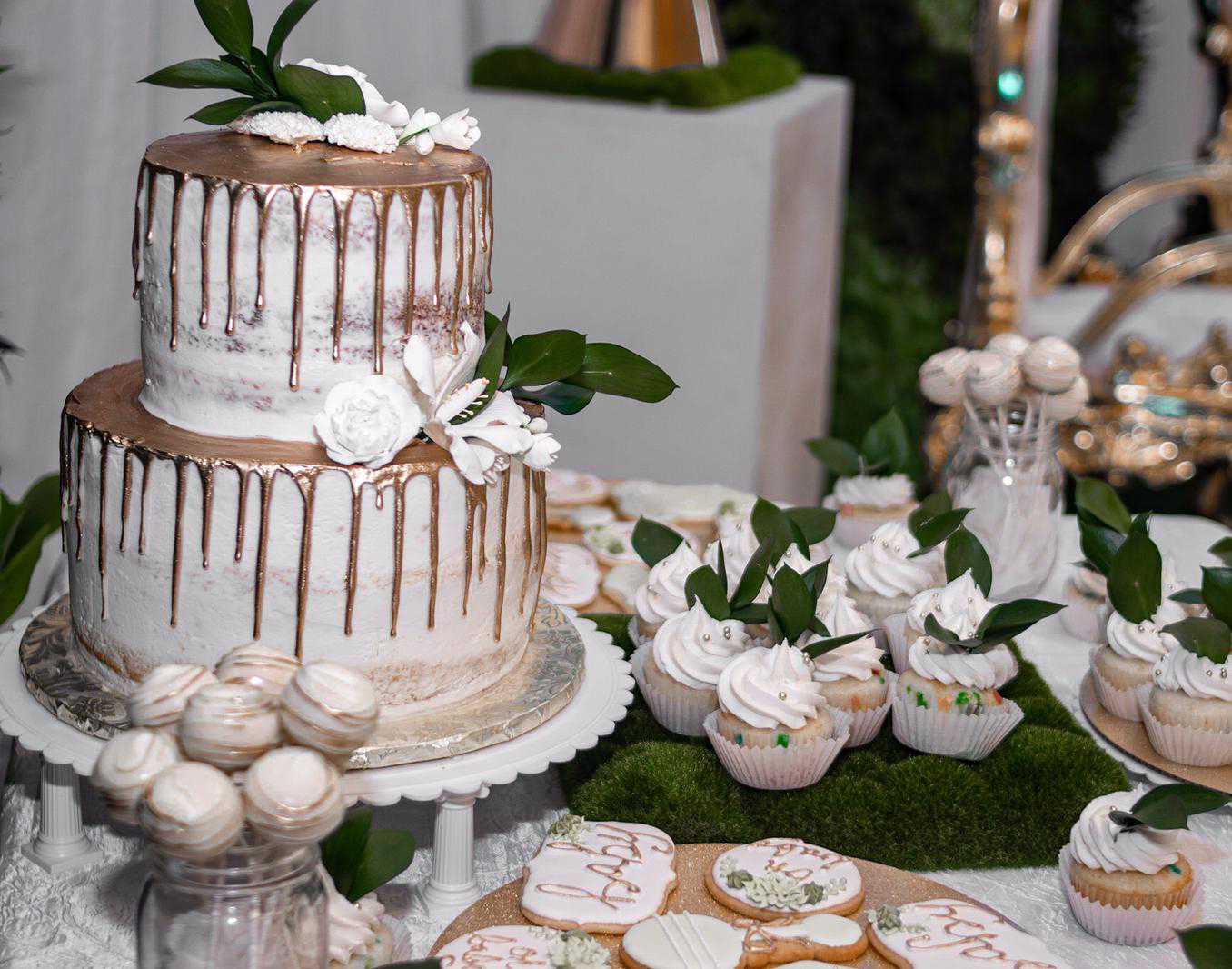 Elegant white and gold wedding cake alongside cupcakes, cookies and cake pops