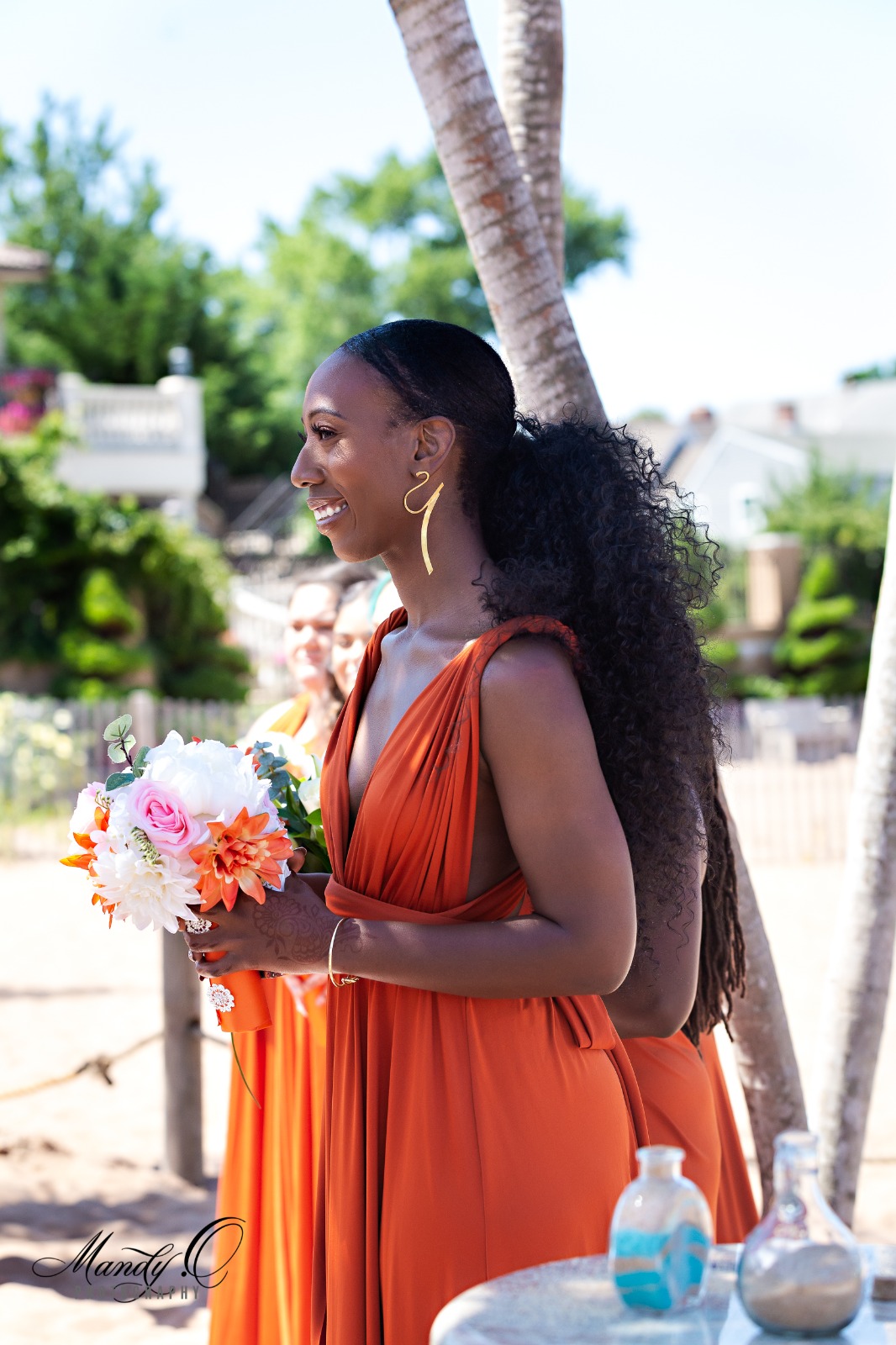 A smilling women in burnt orange, bridesmaid dress with roses.