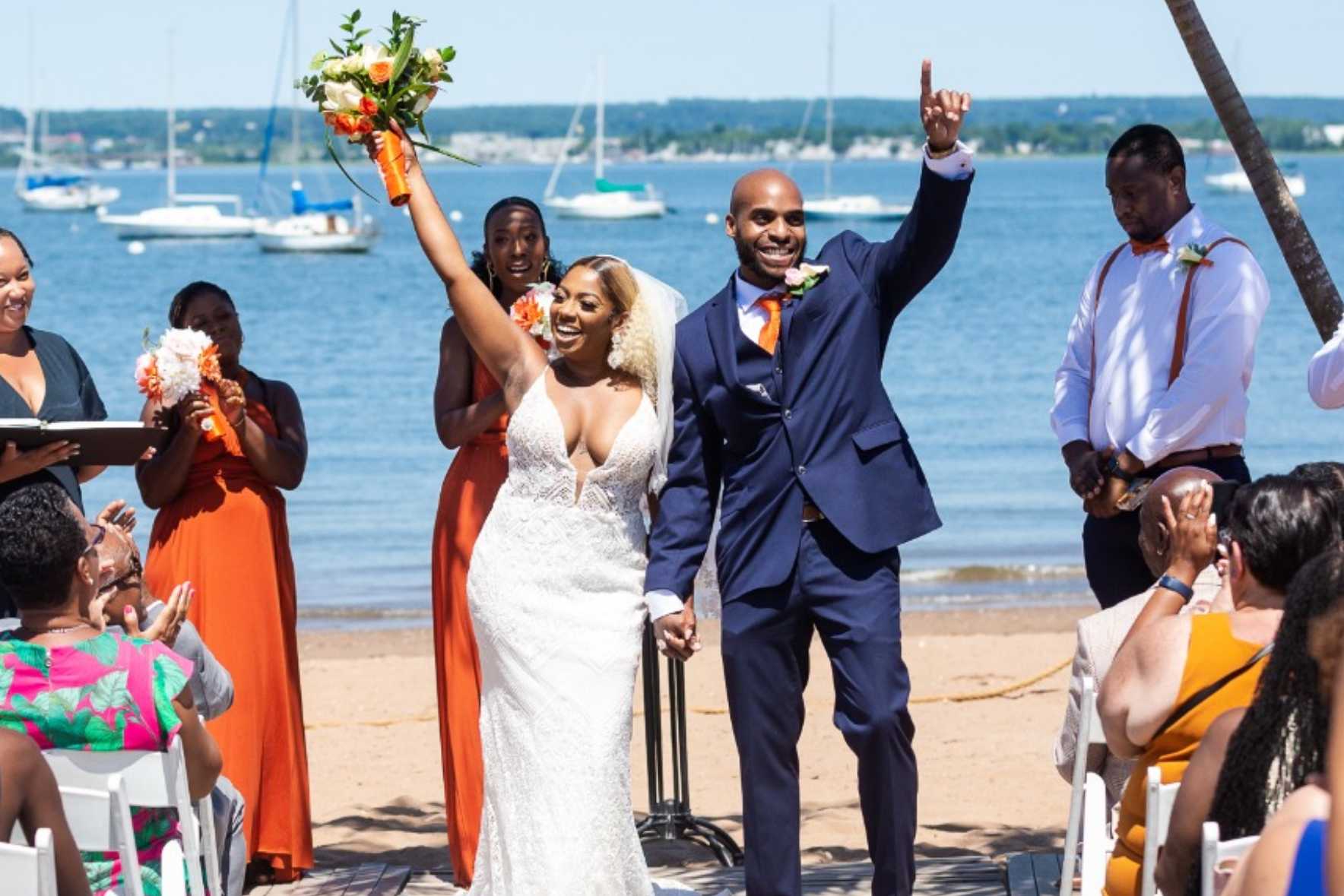 A married couple posing on the beach and people clapping.