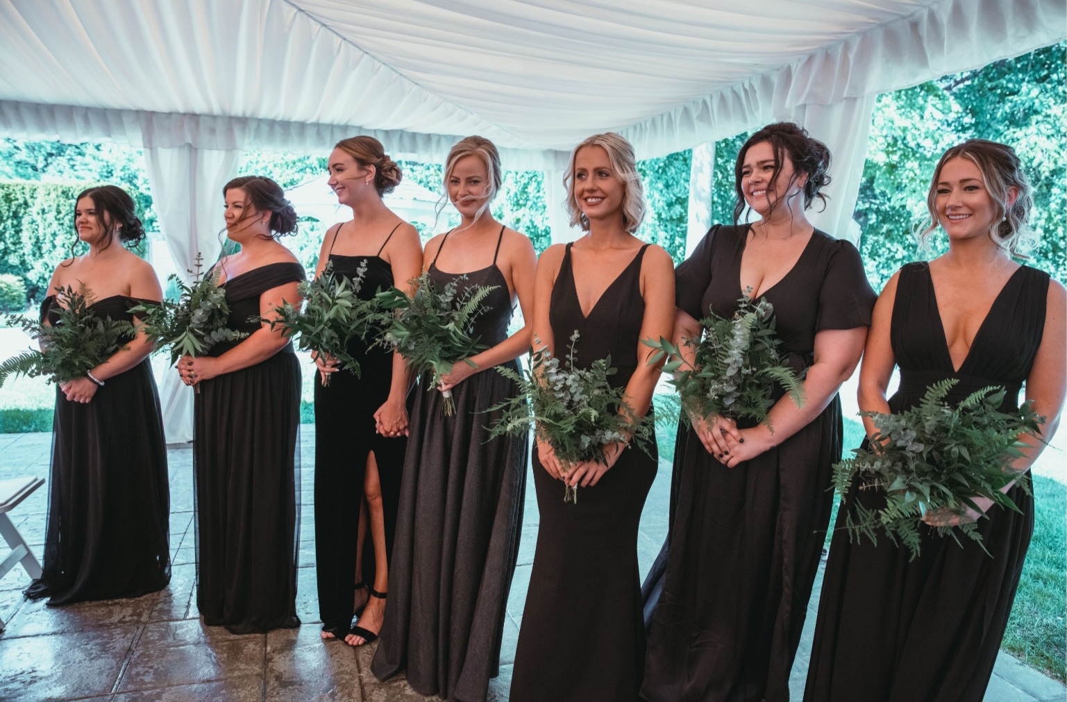 A bridemaids standing on reception with roses in hands in black silk gown.
